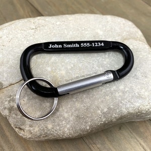 May include: Black carabiner keychain with a silver spring-loaded gate and a silver key ring. The carabiner is engraved with the text "John Smith 555-1234".