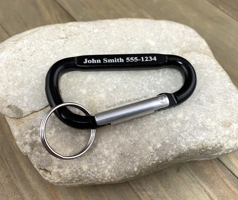 May include: Black carabiner keychain with a silver spring-loaded gate and a silver key ring. The carabiner is engraved with the text "John Smith 555-1234".