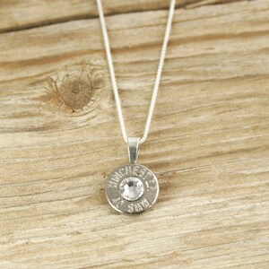 May include: Silver necklace with a round pendant featuring a clear rhinestone and the words "Winchester 30-30" engraved around the edge.