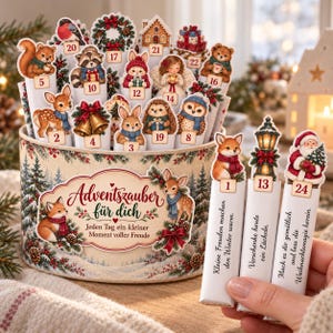 May include: A round decorative container filled with numbered advent calendar sticks featuring illustrations of woodland animals, holiday motifs, and the German text Adventszauber für dich. Each stick displays a unique festive graphic.