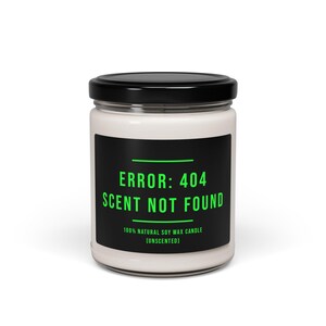 May include: A white unscented soy wax candle in a glass jar with a black lid. The label features the text "ERROR: 404 SCENT NOT FOUND" in green on a black background. The candle is 100% natural.