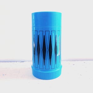 May include: A vintage blue thermos with a black geometric diamond pattern. The thermos has a cylindrical shape with a matching blue lid and base. The design is a retro style.