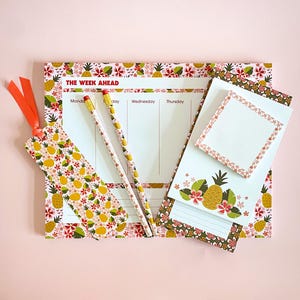 May include: A stationery set with a weekly planner, notepad, sticky notes, a bookmark, and two pencils. The set has a tropical theme with pineapple and floral patterns in yellow, red, and green. The planner reads "THE WEEK AHEAD".