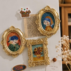 Può includere: Tre cornici dorate decorate contenenti ricami, tra cui un ritratto con foulard blu, un ritratto con cappello blu e pipa, e una natura morta con girasoli. Un adesivo con il testo P294 e un biglietto con scritto Little things make big days.