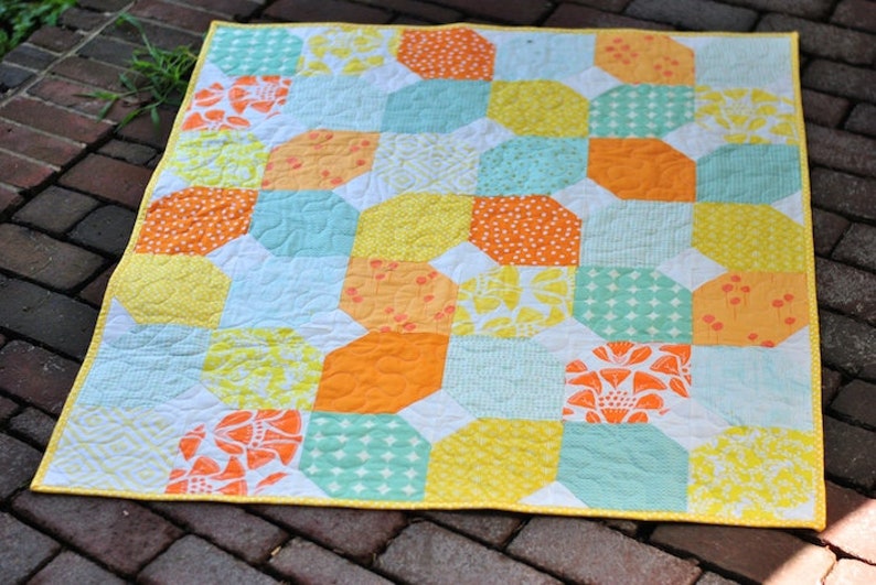 May include: A yellow, orange, and turquoise patchwork quilt with a white background. The quilt is made of various fabrics with different patterns, including polka dots, flowers, and geometric shapes.