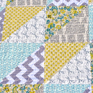 May include: A quilt made of various fabrics in shades of blue, yellow, and gray. The quilt is made up of squares and triangles, and features a pattern of scissors on one of the squares.