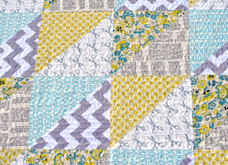 May include: A quilt made of various fabrics in shades of blue, yellow, and gray. The quilt is made up of squares and triangles, and features a pattern of scissors on one of the squares.