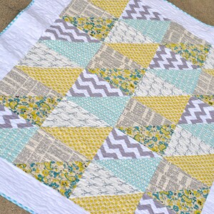 May include: A quilt with a white background and a patchwork design of gray, yellow, and blue triangles. The triangles are made of different fabrics, including a floral print, a newspaper print, and a chevron print.