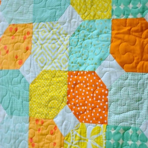 May include: A quilt made of various fabrics in shades of yellow, orange, and green. The quilt is made up of a repeating pattern of octagons and squares.