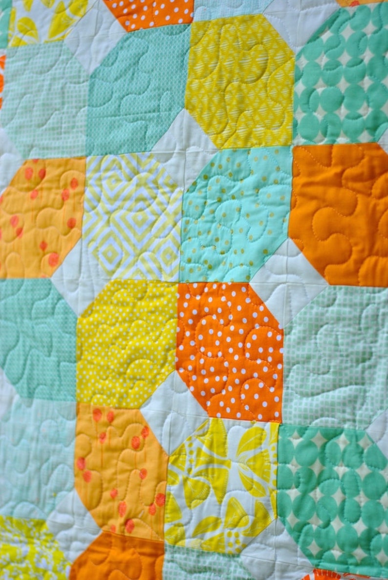 May include: A quilt made of various fabrics in shades of yellow, orange, and green. The quilt is made up of a repeating pattern of octagons and squares.