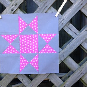 May include: A gray and pink patchwork quilt block with a star design. The star is made up of pink triangles with white stars on them, surrounded by gray squares.