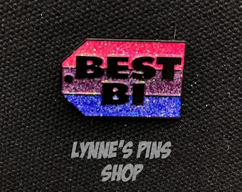 Puede incluir: Un pin rectangular con un acabado brillante, con las palabras "BEST BI" en letras negras. El pin tiene un degradado de color rosa, morado y azul. El texto "LYNNE'S PINS SHOP" está debajo.