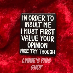 Peut inclure: Épinglette carrée noire avec texte blanc : « IN ORDER TO INSULT ME I MUST FIRST VALUE YOUR OPINION NICE TRY THOUGH ». Le texte « LYNNE'S PINS SHOP » est également présent en bas.