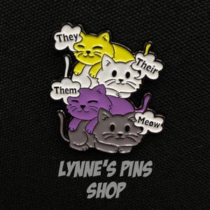 Peut inclure: Épingle en émail colorée représentant quatre chats de dessin animé empilés en jaune, blanc, violet et gris. Chaque chat a une bulle de dialogue avec les mots "They", "Their", "Them" et "Meow". L'épingle porte le texte "Lynne's Pins Shop" en bas.