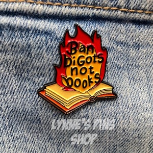 May include: A pin featuring the text "Ban bigots not books" in red and yellow flames above an open book. The pin is set against a denim background. The shop name "Lynne's Pins Shop" is at the bottom.