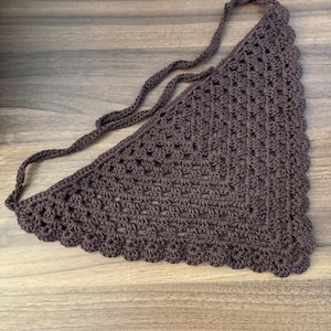 May include: A brown crochet bandana with a scalloped edge and long ties. The triangular scarf is made of a textured, open-weave fabric. The bandana is designed to be tied around the neck or head.