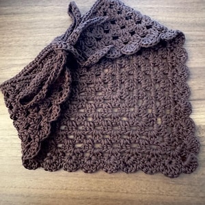 May include: A handmade, dark brown crocheted bag with a scalloped edge. The bag features a drawstring closure and a textured, open weave pattern. The crochet work is detailed and the color is a deep, earthy tone.