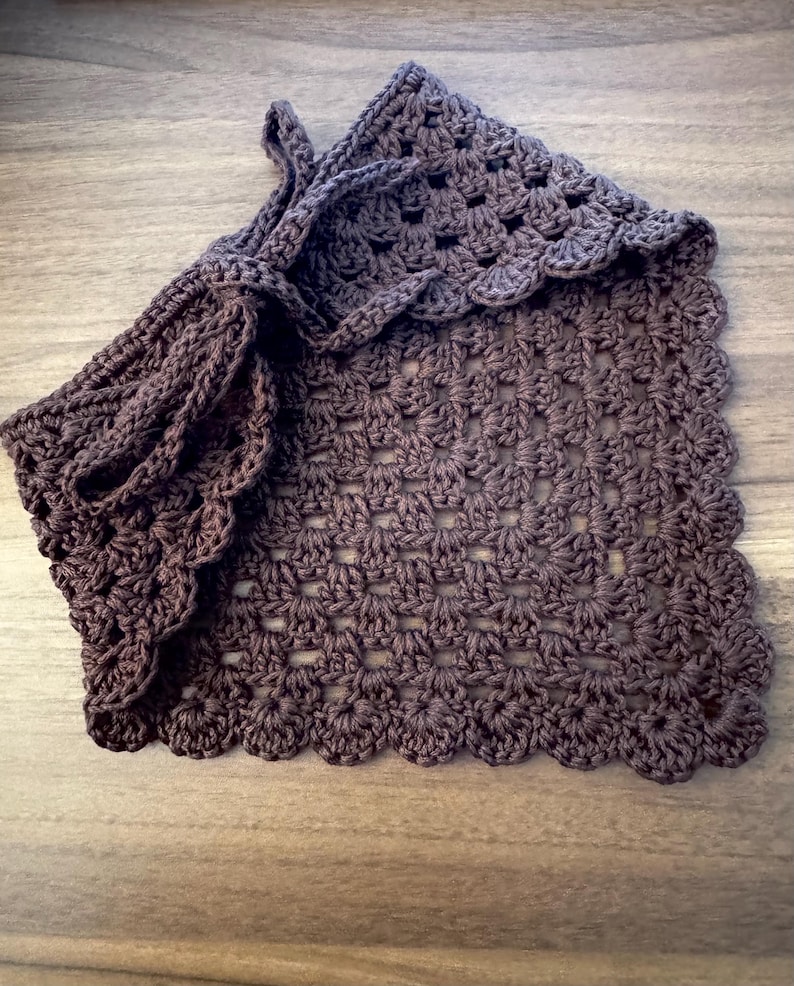 May include: A handmade, dark brown crocheted bag with a scalloped edge. The bag features a drawstring closure and a textured, open weave pattern. The crochet work is detailed and the color is a deep, earthy tone.