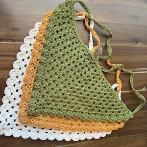 May include: Three crochet tops in a stack. The top layer is a green triangle top with tie straps. Underneath is an orange top, and the bottom layer is a white top. All three tops have a scalloped edge.