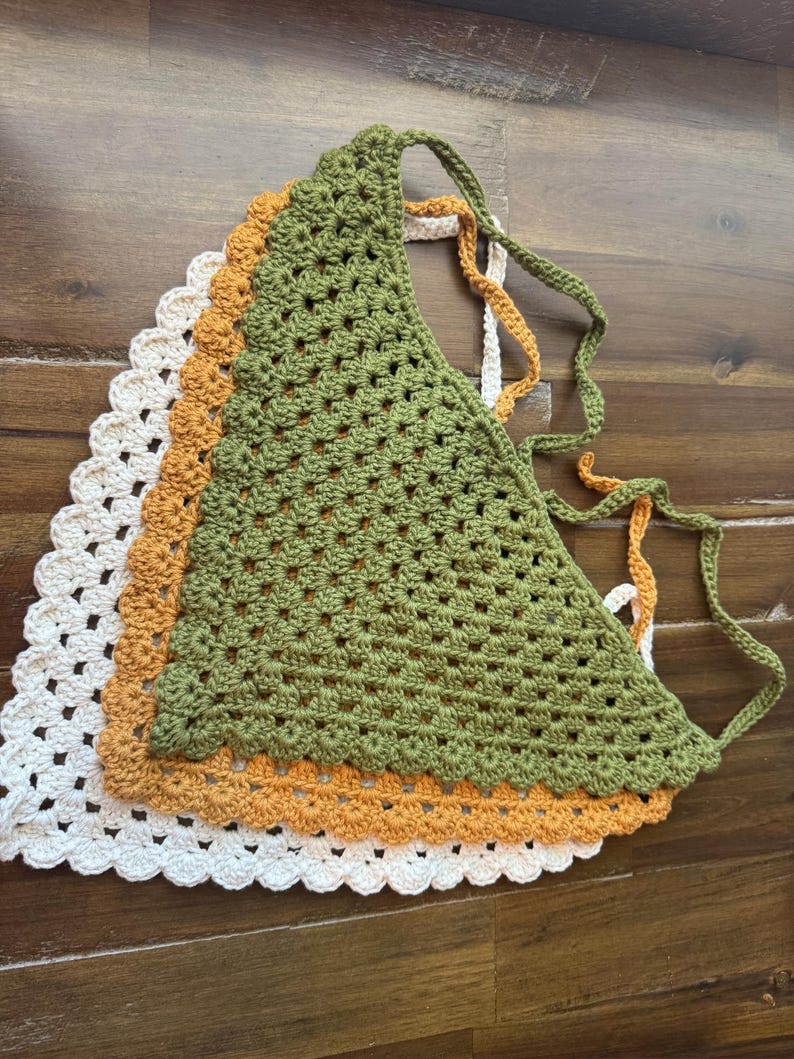 May include: Three crochet tops in a stack. The top layer is a green triangle top with tie straps. Underneath is an orange top, and the bottom layer is a white top. All three tops have a scalloped edge.