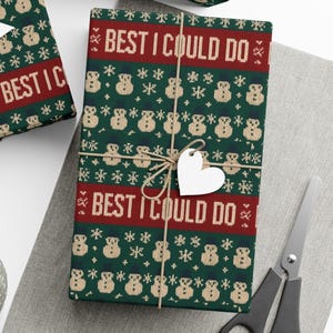 May include: Wrapped gift with green wrapping paper featuring a repeating pattern of snowmen and snowflakes. The text "BEST I COULD DO" is printed in red. A heart-shaped tag is tied to the gift with twine.