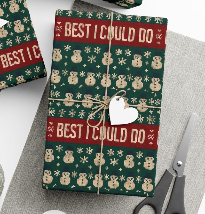 May include: Wrapped gift with green wrapping paper featuring a repeating pattern of snowmen and snowflakes. The text "BEST I COULD DO" is printed in red. A heart-shaped tag is tied to the gift with twine.