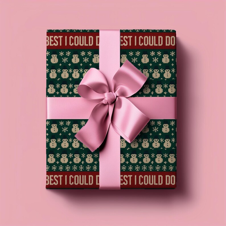 May include: A wrapped gift with a green and red patterned paper featuring snowmen and snowflakes. The text "BEST I COULD DO" is printed on the paper. A pink satin ribbon and bow are tied around the gift.