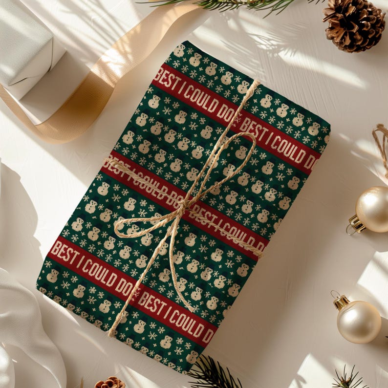 May include: A wrapped gift with green wrapping paper featuring a repeating pattern of snowmen and snowflakes. The words "BEST I COULD DO" are printed in red. The gift is tied with twine and is surrounded by Christmas ornaments.