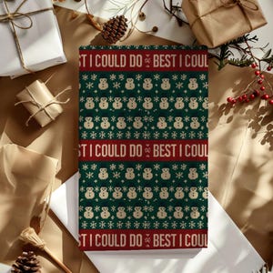 May include: A rectangular gift wrapped in green paper with a repeating pattern of snowmen and snowflakes. The design includes the text "ST I COULD DO BEST I COUL" in red. The gift is surrounded by other wrapped presents.