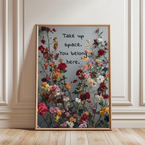 Puede incluir: Un estampado floral enmarcado con una variedad de flores coloridas en tonos de rojo, rosa, amarillo y naranja sobre un fondo gris. El estampado incluye el texto "Take up space. You belong here."