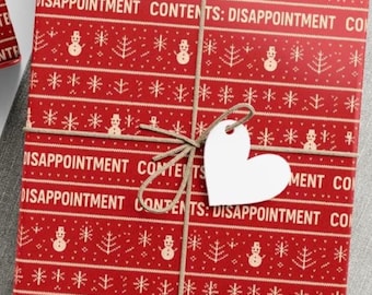 May include: A wrapped gift with red wrapping paper featuring a repeating pattern of snowmen, Christmas trees, and the text "DISAPPOINTMENT CONTENTS". The gift is tied with twine and has a white heart-shaped tag.