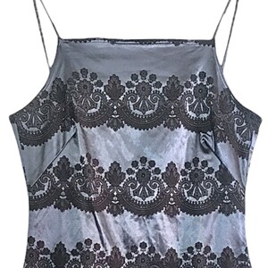 Puede incluir: Una blusa de sat&eacute;n gris sin mangas con un patr&oacute;n de encaje negro. El patr&oacute;n de encaje es un dise&ntilde;o repetitivo de espirales y flores.