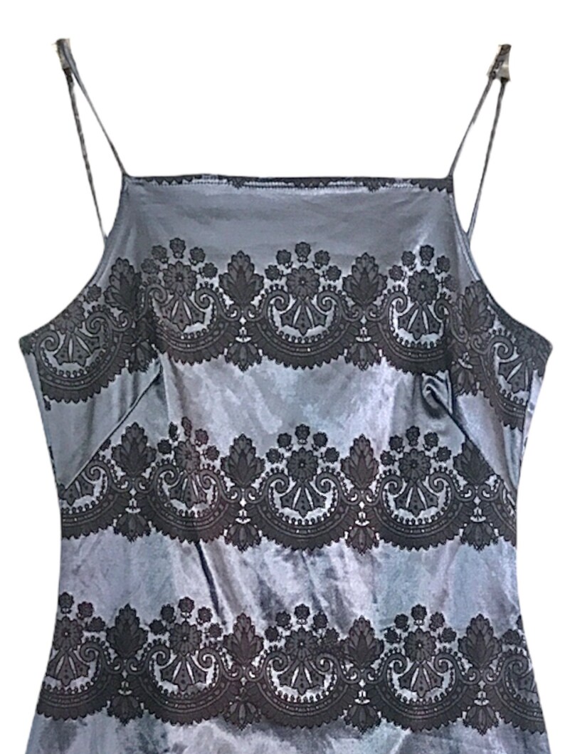 Puede incluir: Una blusa de sat&eacute;n gris sin mangas con un patr&oacute;n de encaje negro. El patr&oacute;n de encaje es un dise&ntilde;o repetitivo de espirales y flores.