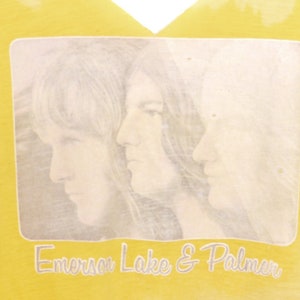 May include: Yellow t-shirt with a faded image of three people and the text "Emerson Lake & Palmer" printed on the front.