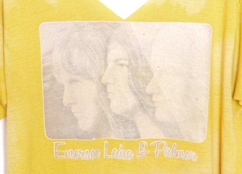 May include: Yellow t-shirt with a faded image of three people and the text "Emerson Lake & Palmer" printed on the front.