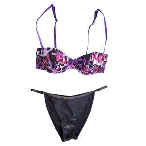 May include: A two-piece lingerie set. The bra features a purple, pink, and black patterned design with adjustable purple straps. The matching thong is black with a thin waistband.