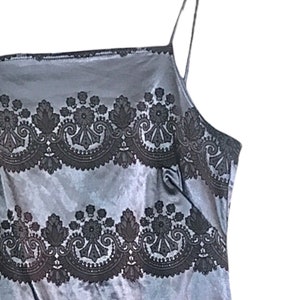 Puede incluir: Un vestido de sat&eacute;n gris sin mangas con un patr&oacute;n de encaje negro. El vestido tiene un escote cuadrado y tirantes finos.