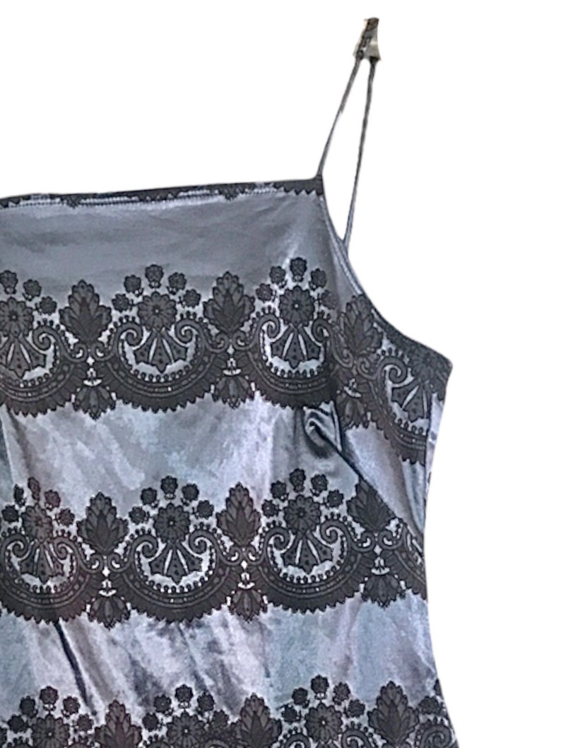 Puede incluir: Un vestido de sat&eacute;n gris sin mangas con un patr&oacute;n de encaje negro. El vestido tiene un escote cuadrado y tirantes finos.
