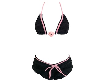 May include: Black bikini set with pink trim and a small flower accent. The top is a triangle style with halter straps. The bottoms are ruched with a tie detail. The swimwear is designed for a comfortable fit.