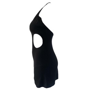 May include: A black halter dress with a side cutout. The dress is sleeveless and has a fitted silhouette. The cutout is a large oval shape. The dress is made of a smooth, solid fabric.