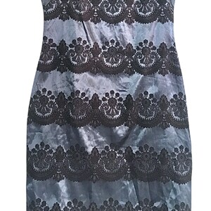 Puede incluir: Un vestido sin mangas con fondo azul y ribete de encaje negro. El ribete de encaje es un patr&oacute;n repetido de dise&ntilde;os florales y paisley.