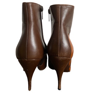 May include: A pair of brown leather ankle boots with stiletto heels. The boots have a zipper closure on the side and a pointed toe. One boot has a patch of tan leather on the side.
