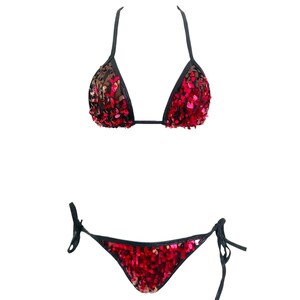 May include: A two-piece bikini set featuring a triangle top and tie-side bottoms. The garment is covered in vibrant red and black sequins, with black trim along the edges of the cups and the waistband. The top has thin black shoulder straps.