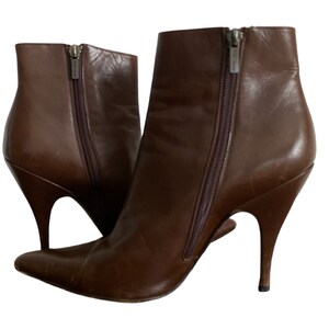 May include: A pair of brown leather ankle boots with pointed toes and stiletto heels. The boots have side zippers and a sleek, modern design. The heels are approximately 4 inches high.