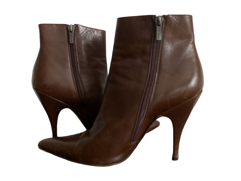 May include: A pair of brown leather ankle boots with pointed toes and stiletto heels. The boots have side zippers and a sleek, modern design. The heels are approximately 4 inches high.