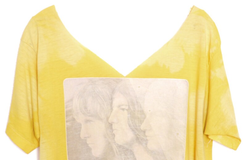 May include: Yellow t-shirt with a faded image of three people with long hair. The image is in a white rectangle.