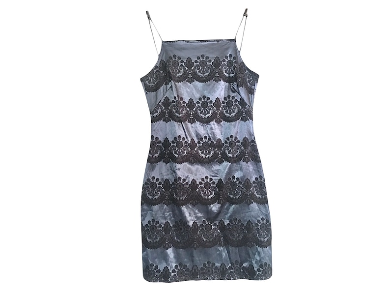 Puede incluir: Un vestido de sat&eacute;n gris sin mangas con ribete de encaje negro. El vestido tiene una silueta ajustada y un escote recto.