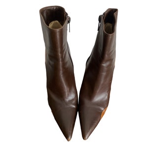May include: A pair of brown leather ankle boots with pointed toes. The boots have a zipper on the side and a small heel. The leather has a glossy finish. The boots are set against a white background.