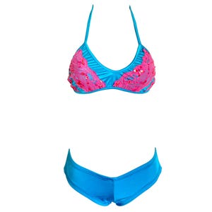 May include: A two-piece swimsuit set in bright turquoise blue. The top features a halter neck and is embellished with pink lace and sequins. The matching bottoms are a low-rise style. The swimsuit is designed for swimwear.