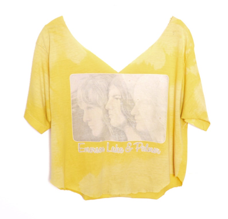 May include: A yellow cropped t-shirt with a faded tie-dye pattern. The shirt features a black and white image of three people with the text "Emerson Lake & Palmer" printed below the image.